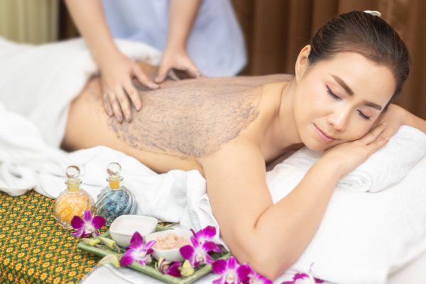 beautiful young Asian woman relaxing with hand massage making mud clay mask and salt scrub on naked back body skin by masseur at beauty spa salon treatment. relaxing massage